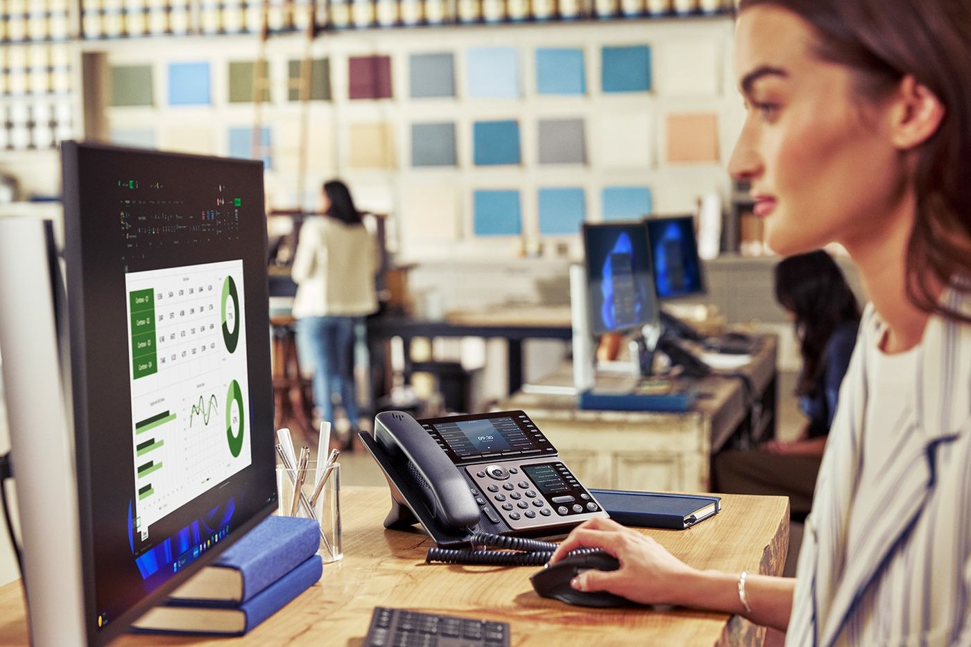 Woman at desk with HP Poly Edge desk phone and monitor in a bright office